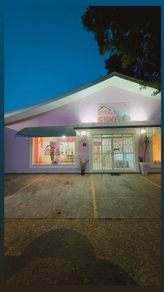 Fachada da Casa do Brigadeiro ao entardecer, com letreiro iluminado e vitrine acolhedora